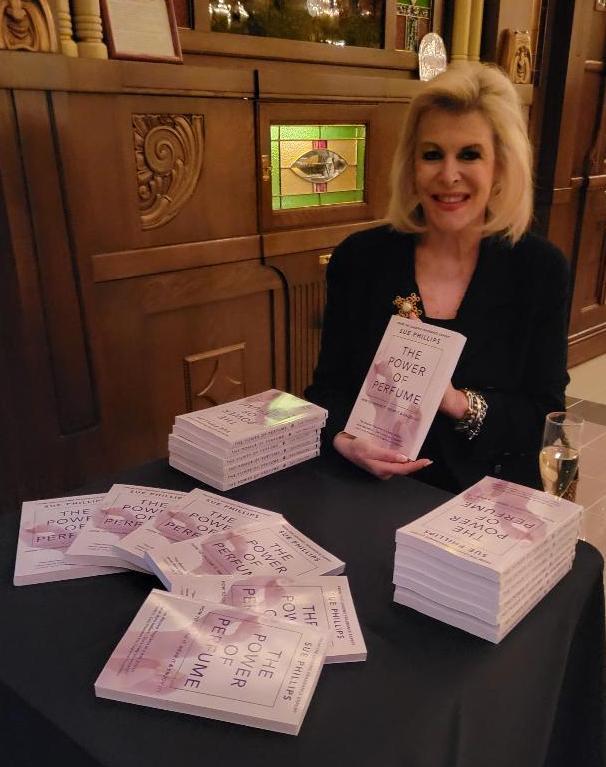 Sue Phillips holding a copy of her recently published The Power of Perfume during book signing.